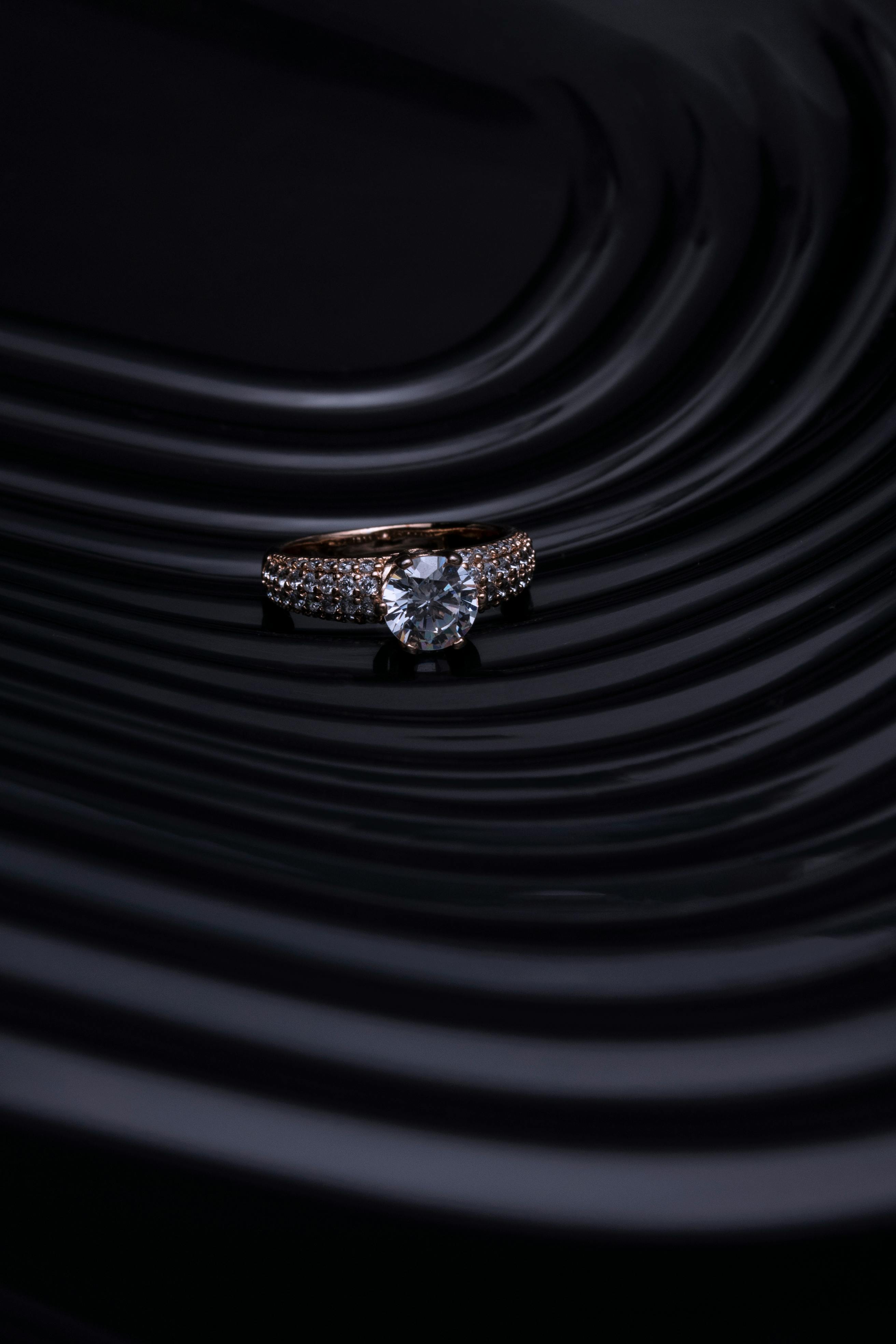 Close Up Of A Diamond Ring With A Dark, Wavy Background Creating A Luxurious And Elegant Atmosphere.